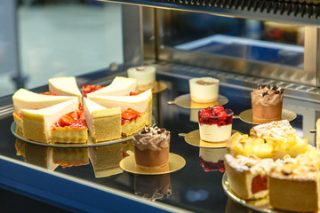 Many different cakes are on the counter of a pastry shop.