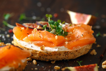 Salmon Bagel Sandwich with figs, cress salad, walnuts, cream cheese and grain on rustic wooden background. healthy breakfast