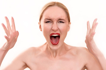 Beautiful blonde woman with pretty blue eyes and red lips. A scary female in pain holding her head and screaming in anger with an open mouth on her menstrual cycle period pain