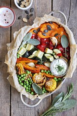 Roasted vegetables in serving pan on a rustic wooden table. Overhead view.