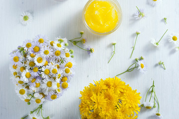cosmetic product samples with herbal flowers on white wooden table