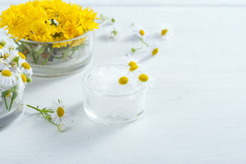 cosmetic product samples with herbal flowers on white wooden table