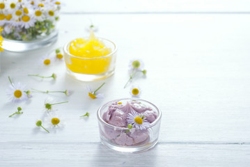 cosmetic product samples with herbal flowers on white wooden table