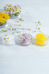 cosmetic product samples with herbal flowers on white wooden table
