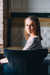 Beautiful young woman sits near big window at cafe, and looking at the camera.