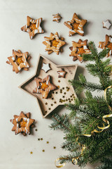 Homemade Christmas star shape sugar caramel cookies with frosting and orange citrus jam in wooden plate over white marble background with fir branches. Flat lay, space. Sweet xmas or new year gift.