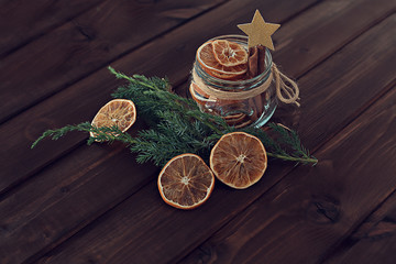 dried orange slices in a jar with a branch of a Christmas tree on a wooden background with gold star decoration