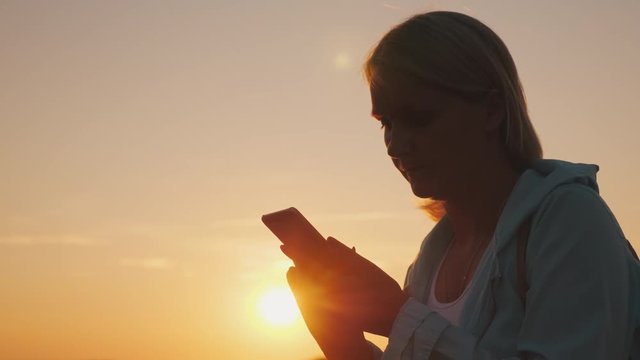 Silhouette Of A Middle-aged Woman Using A Smartphone At Sunset