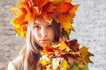 Naklejka na ściany i meble portrait of young teenager brunette girl with long hair with a wreath of autumn leaves on her head on gray wall background