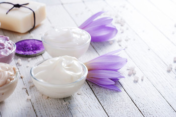 Fototapeta na wymiar cosmetic cream variations, soap and bath salt with autumn crocus herbal flower on white wooden table