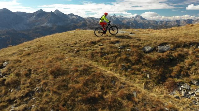 4K sport footage, aerial view one man riding electric mountain bike over ridge high up in mountains panorama on sunny autumn day
