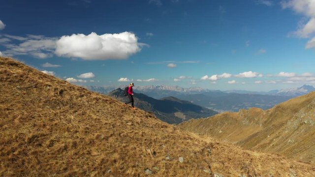 4K sport footage, aerial drone view one 40 years old woman hiking alone on mountain ridge high above on sunny day in autumn
