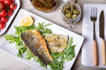 Grilled seabass fillet with arugula, lemon, tomatoes and capers. Close-up.