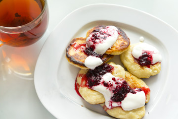 few pancakes with cream sauce and jam on a plate, a Cup of tea
