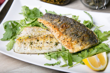 Grilled seabass fillet with arugula and lemon. Close-up.