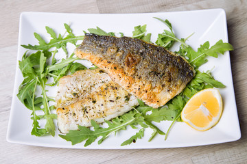 Grilled seabass fillet with arugula and lemon. Close-up.