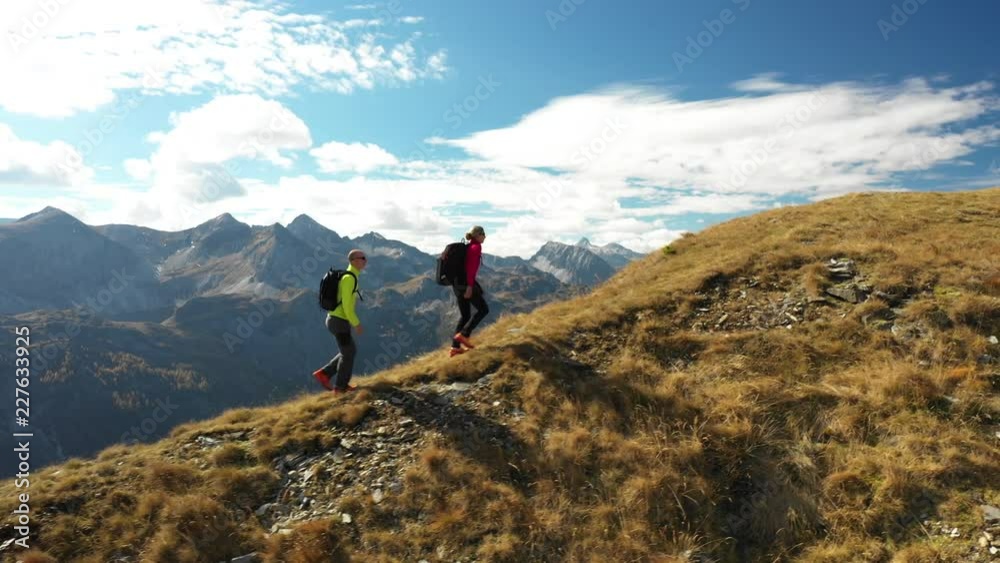 Wall mural 4k sport footage, aerial drone view active people couple hiking on mountain ridge on sunny day in au