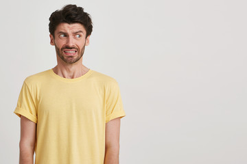 Clouse up of afraid fearful young man with dark brown hair and beard wears yellow casual tshirt, look right, standing left side isolated over white background - obrazy, fototapety, plakaty