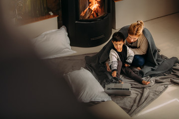 Mother and son with laptop near fireplace