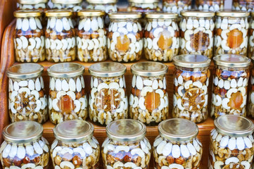 Glass jars with different nuts, dried apricots and figs filled with honey are on wooden shelves at the food exhibition