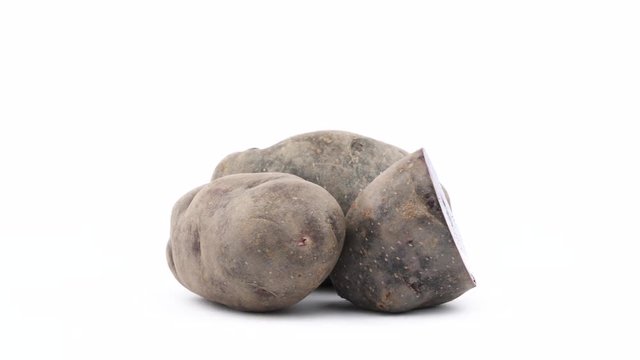 Two whole violet potatoes and one-half of vitelotte potato. Rotating on the turntable isolated on the white background. Close up. Macro.