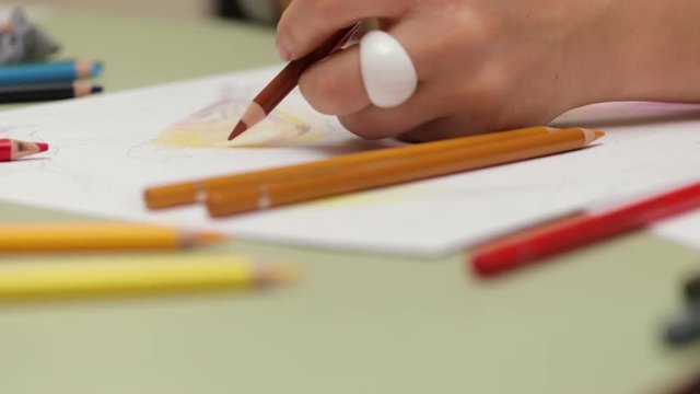 Girl draws left-handed with colored pencil on paper, detailed view in slowmotion