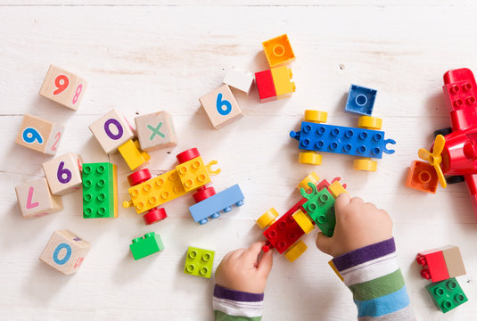 Child playing with wooden cubes with numbers and colorful toy bricks on a white wooden background. Toddler learning numbers. Hand of a child taking toys.