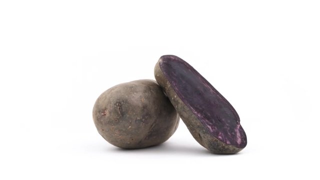 One whole vitelotte potato, one half of violet potato. Slowly rotating on the turntable isolated on the white background. Close up. Macro.