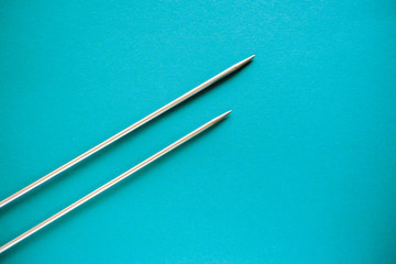 Long iron knitting needles on light blue background.