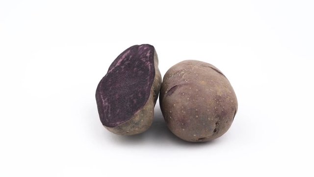 One half and one whole vitelotte potato. Slowly rotating on the turntable isolated on the white background. Close up. Macro.