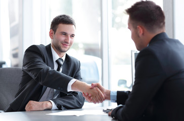 handshake of business partners sitting at a Desk