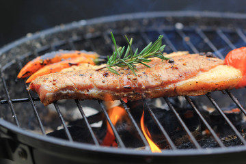 Beef steaks with rosemary on grill with flame and smoke on dark background, food meat or barbecue