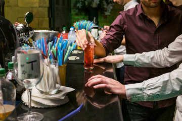Two man  are standing at a bar counter and holding  glass with an alcoholic cocktail  Red cocktail in a glass at a nightclub, beach, restaurant