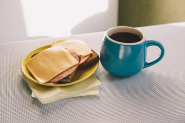 Blue cup of coffee with cheese sandwiches on the table in morning, simple lunch or breakfast