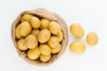 Sack of fresh raw potatoes on wooden background, top view