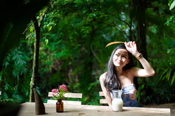 Asian pretty girl has drinkling ice white milk with happy and smiling at Little Tree Garden cafe, Nakhon Pathom province, Thailand in the morning.