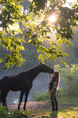 Young woman with her horse on a beautiful landscape. Clear lake at morning fog. Sunrise