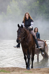 Two young women on horses goes out of the lake