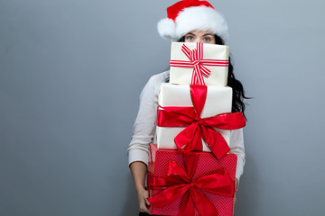 Young woman with santa hat holding gift boxes on a gray background