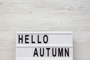 Modern board with text 'Hello Autumn' on a white wooden background, overhead view. Top view, flat lay, from above. Copy space.