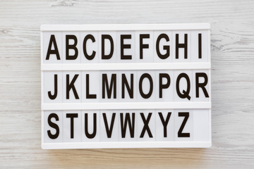English alphabet on lightbox over white wooden background, overhead view. Letters from A to Z. Back...