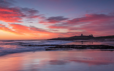 Sunrise over Dunstanburgh Castle on the coast of Northumberland, England, UK.