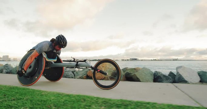 Disabled wheelchair athlete pushing racing chair outside at sunset working out 