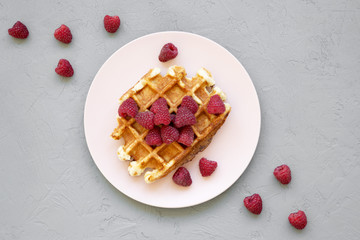 Traditional belgian waffle with raspberries on pink plate over concrete background, view from above. Close-up.