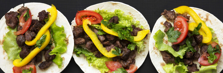 Corn tortillas with beef and vegetables on black background, top view. Mexican cuisine. Flat lay, from above.