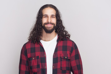 Portrait of happy handsome man with beard and black long curly hair in casual style, checkered red...