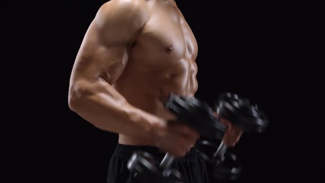Man flexes his hands with dumbbells, training his biceps on a black background in the studio