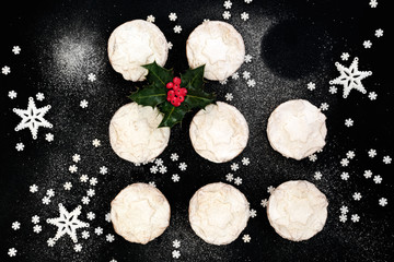 Delicious freshly baked Christmas mince pies with one missing, holly berry leaf sprig, star decorations and icing sugar dusting on black background. Top view.