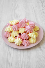 Fototapeta na wymiar Mini meringues on pink plate on white wooden table, low angle view.