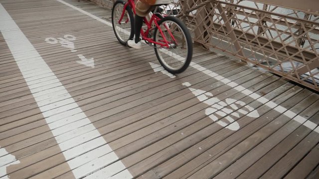 A slow motion low angle view of bicyclists in the bike lane on the Brooklyn Bridge on an overcast day.  	